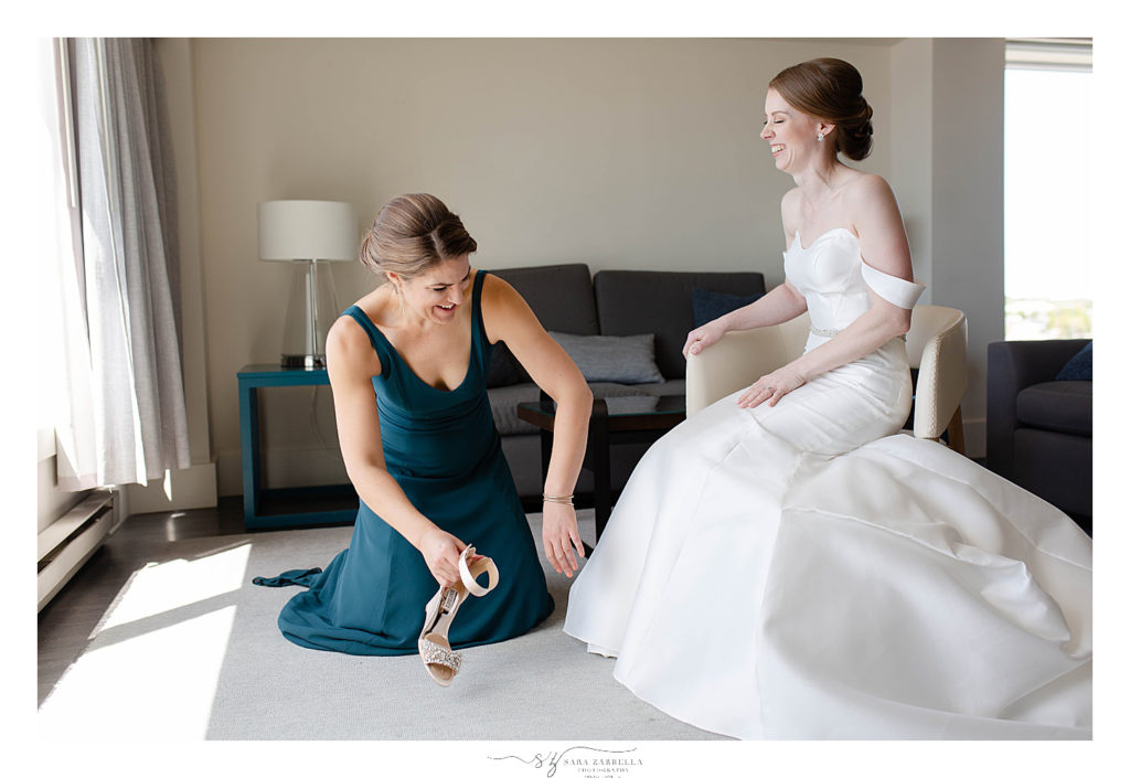 bridesmaid helps bride into shoes on wedding day with Sara Zarrella Photography
