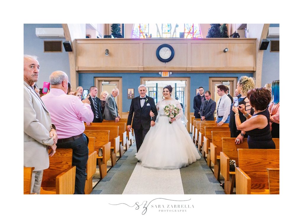 bride walks down aisle at church with Sara Zarrella Photography