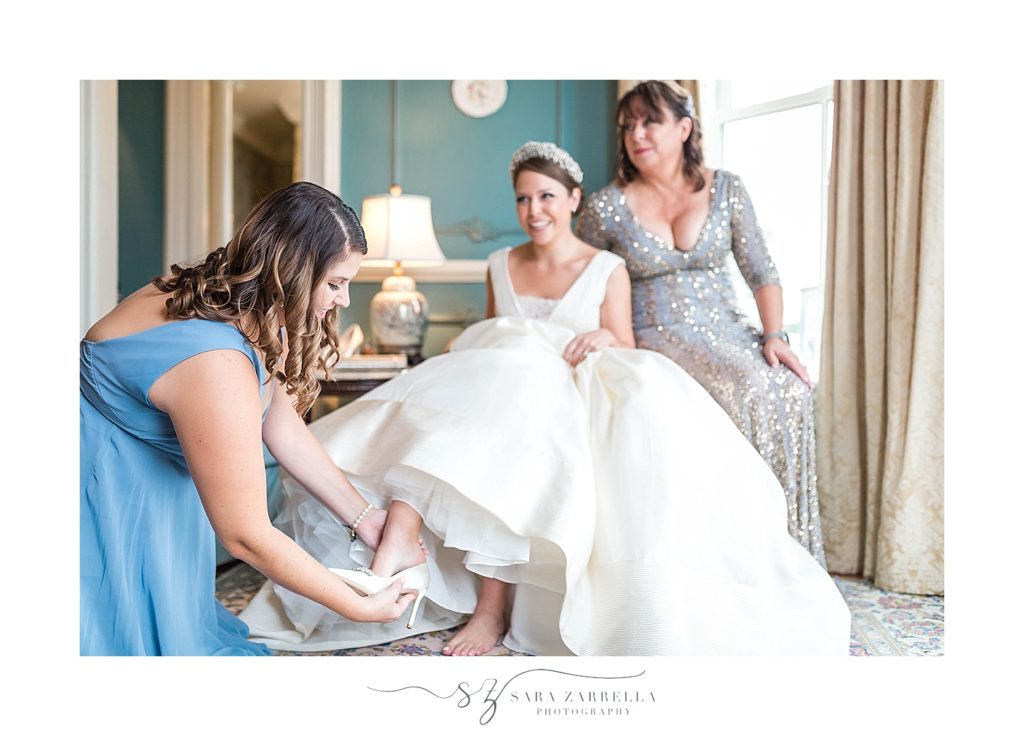 bridesmaid helps bride into shoe on wedding day with Sara Zarrella Photography