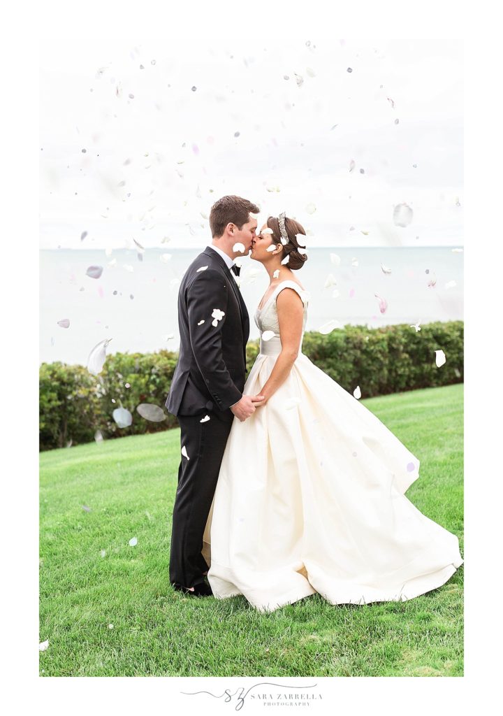 bride and groom kiss while white flower petals fall around them