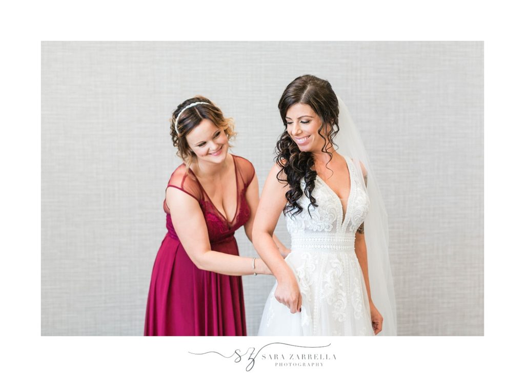 bridesmaid helps bride into wedding dress photographed by Sara Zarrella Photography