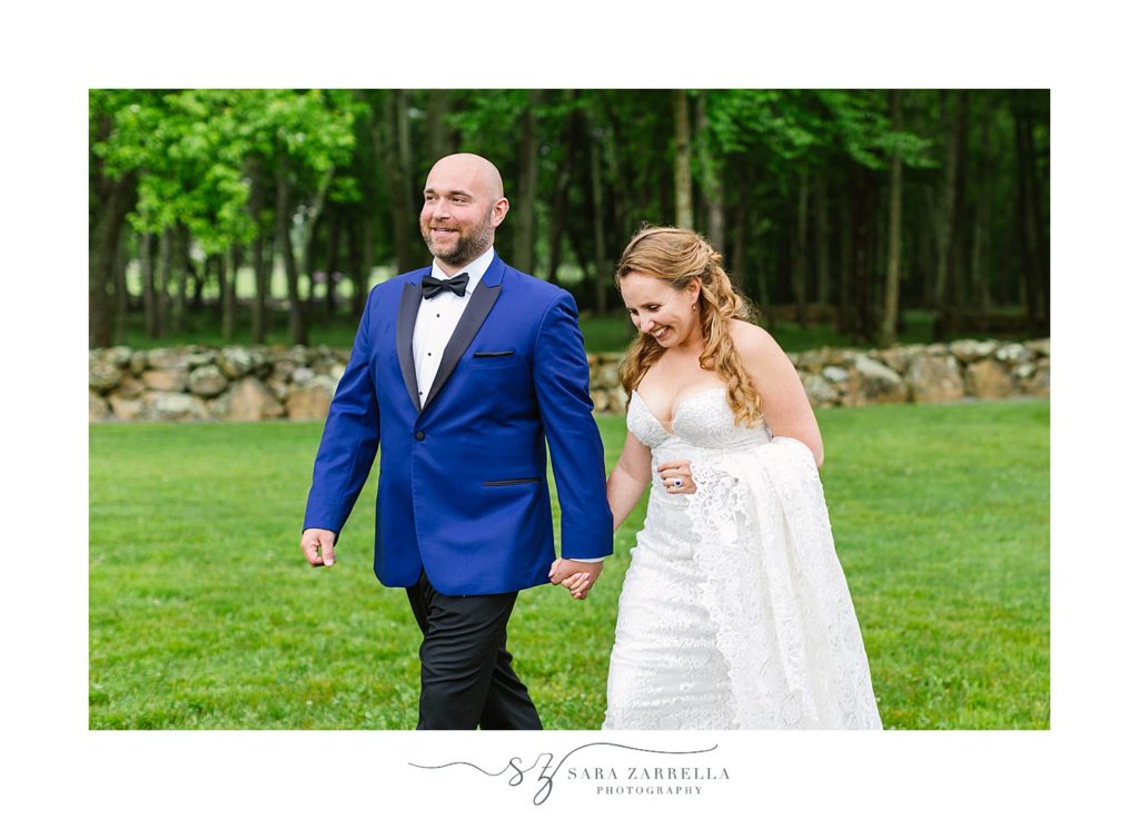 groom in blue tux holds bride's hand and walks at Geral'ds Farm