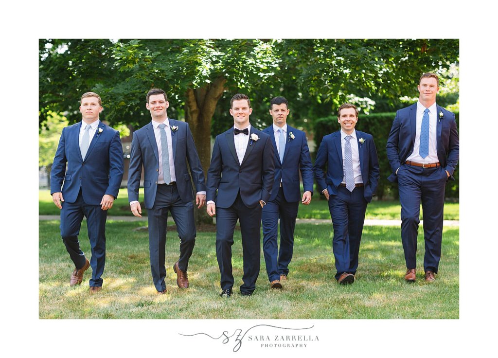 groom and groomsmen in navy suits walk at Providence College