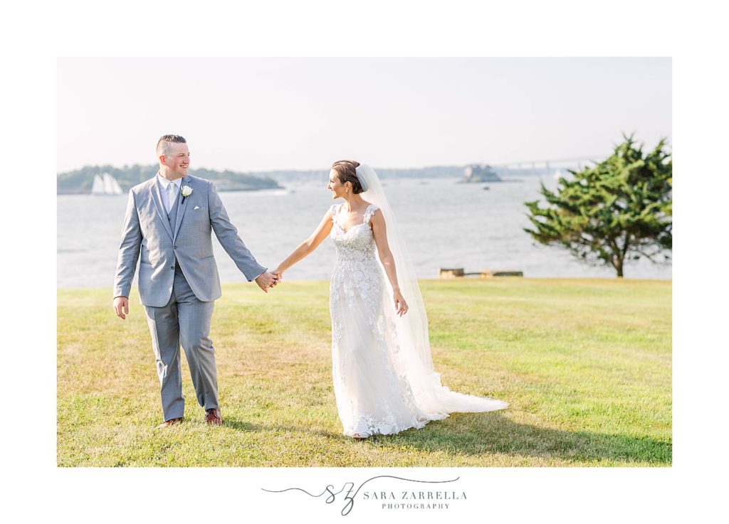newlyweds hold hands and walk along waterfront in Newport Ri