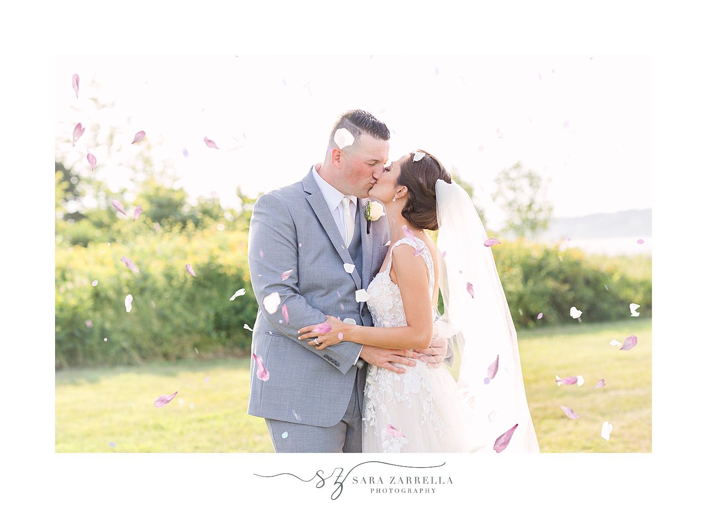 bride and groom kiss while flower petals fall around them