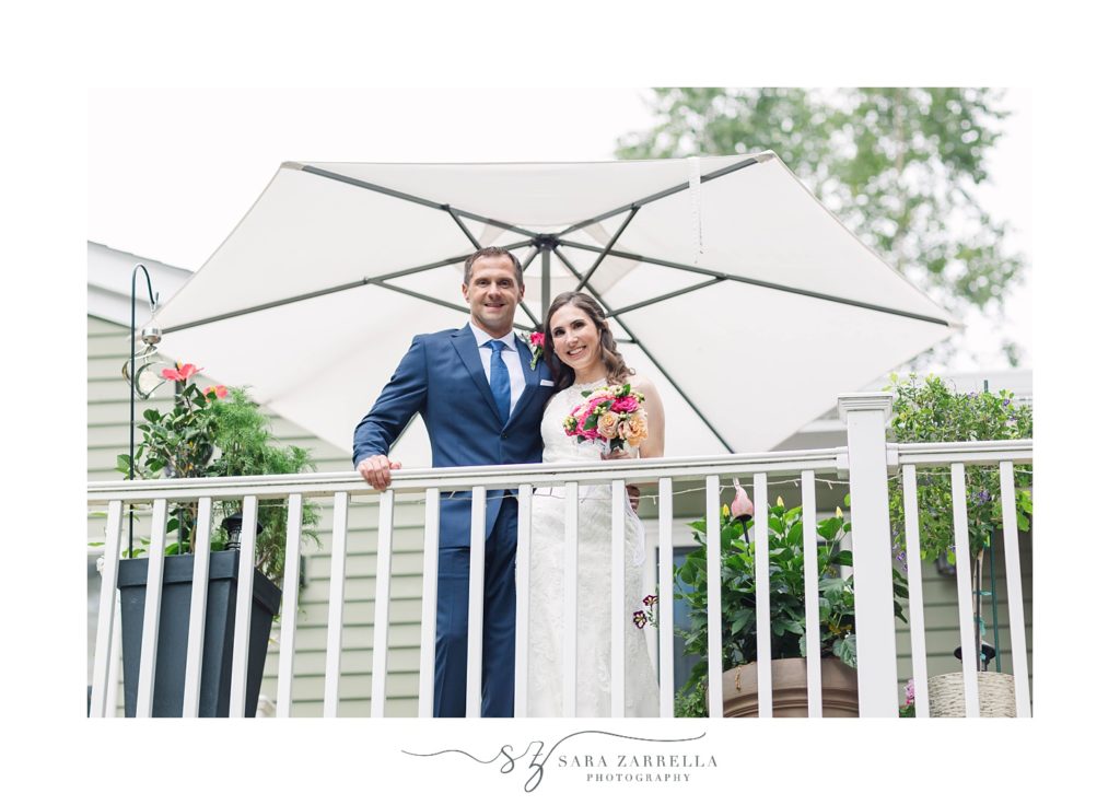 bride and groom pose on deck under white umbrella