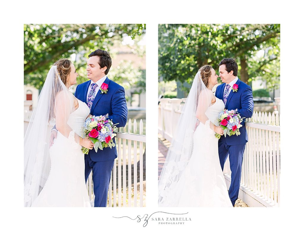 bride and groom pose by white picket fence during Thames Street wedding portraits