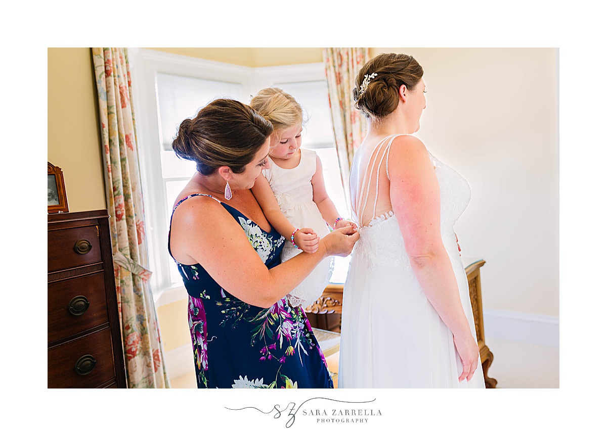 bridesmaid and bride's daughter adjust bride's gown
