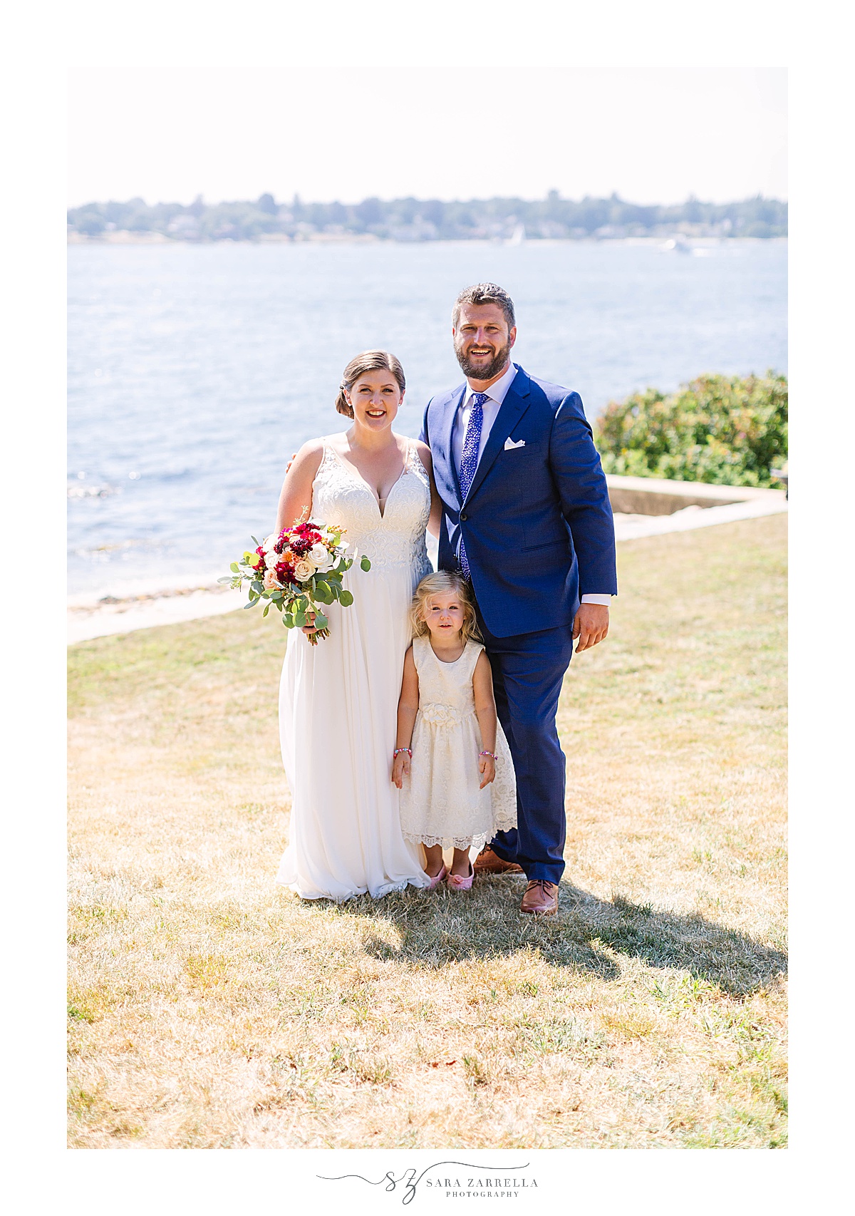 bride and groom pose with daughter on waterfront estate wedding day