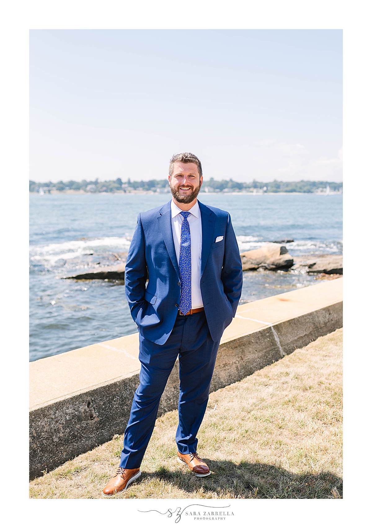 groom in navy suit poses by water in Groton CT