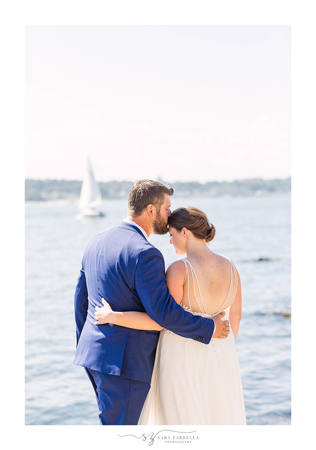 groom kisses bride while they watch sailboat