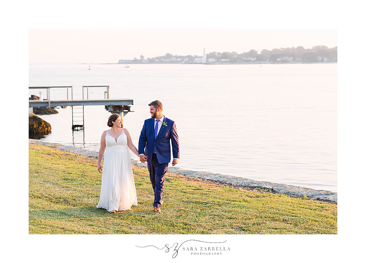 bride and groom walk along water in New England