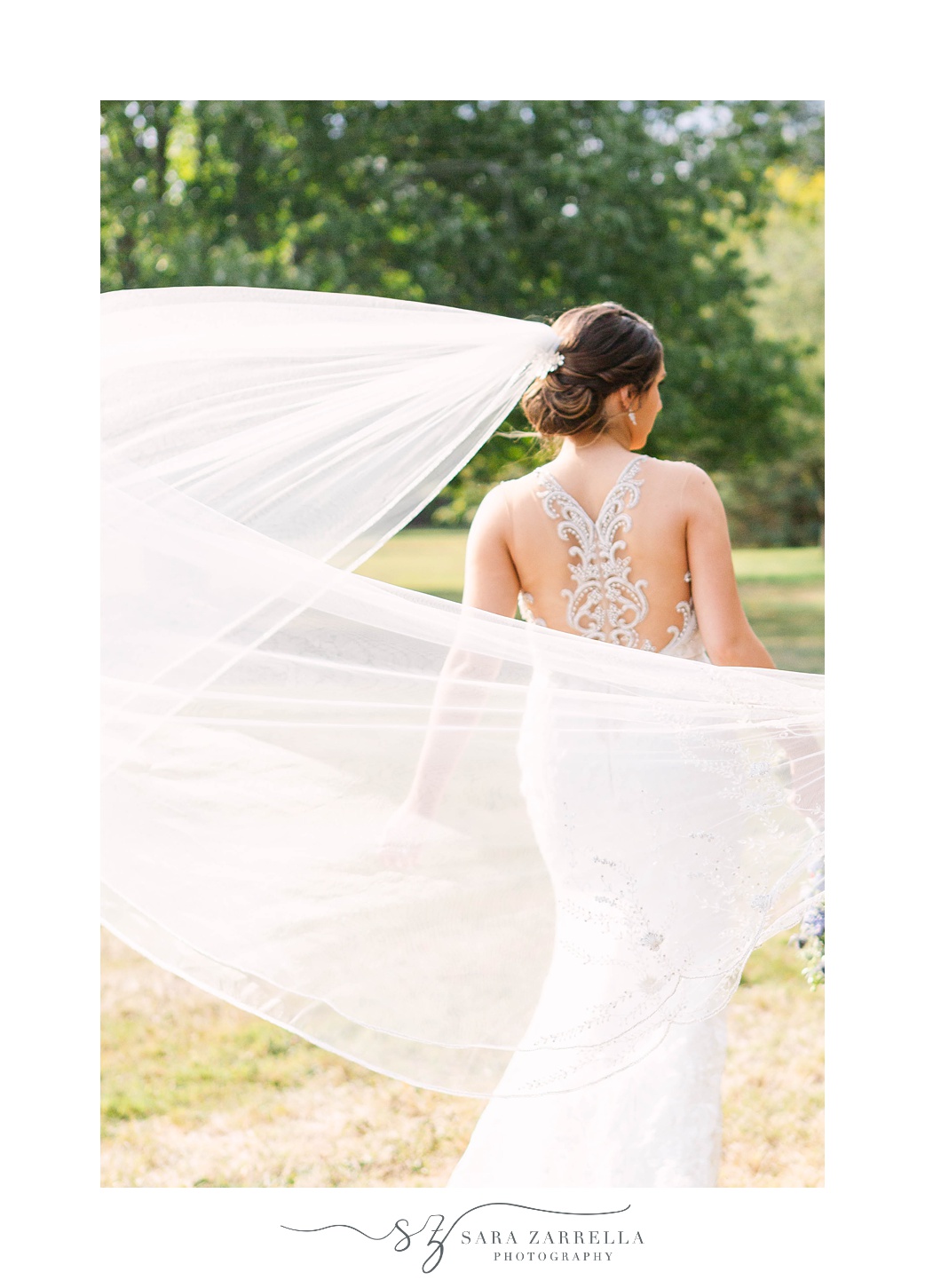bride shows off back of wedding gown with veil
