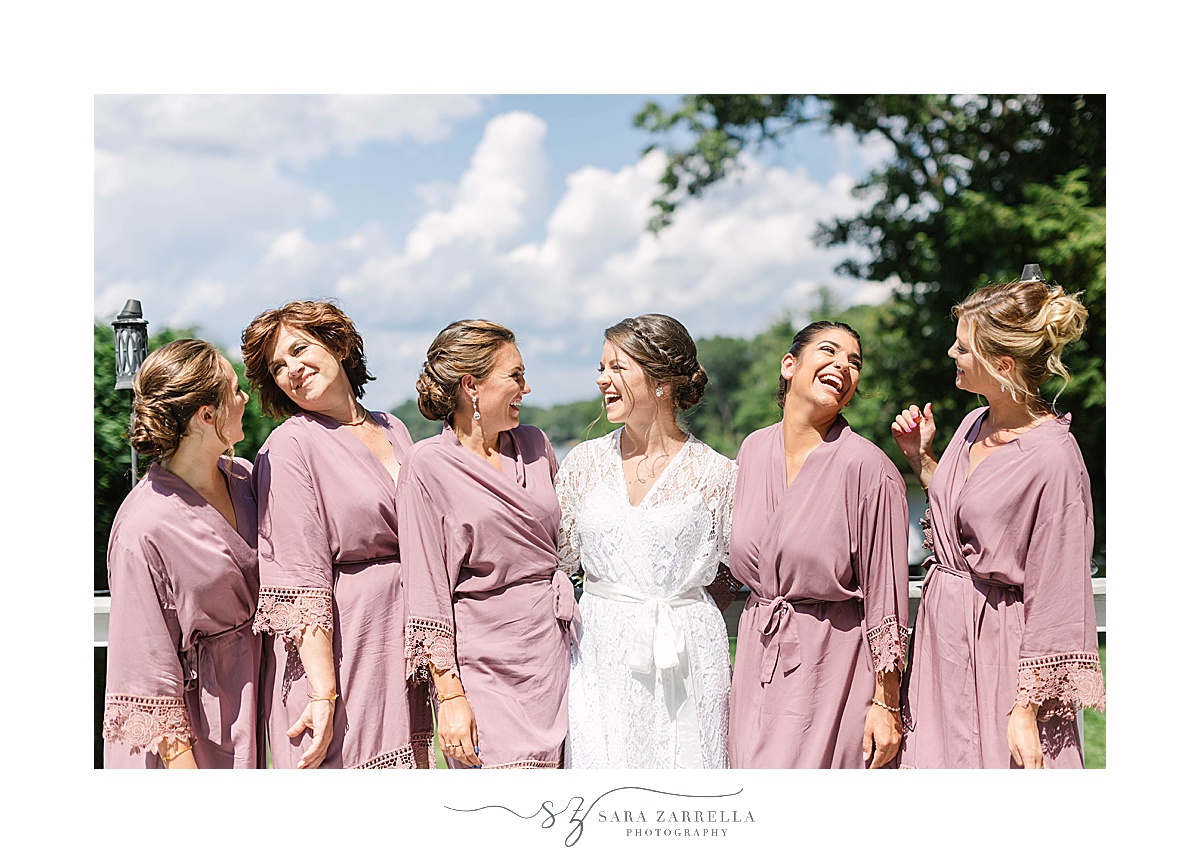 bride poses with bridesmaids before lakeside wedding