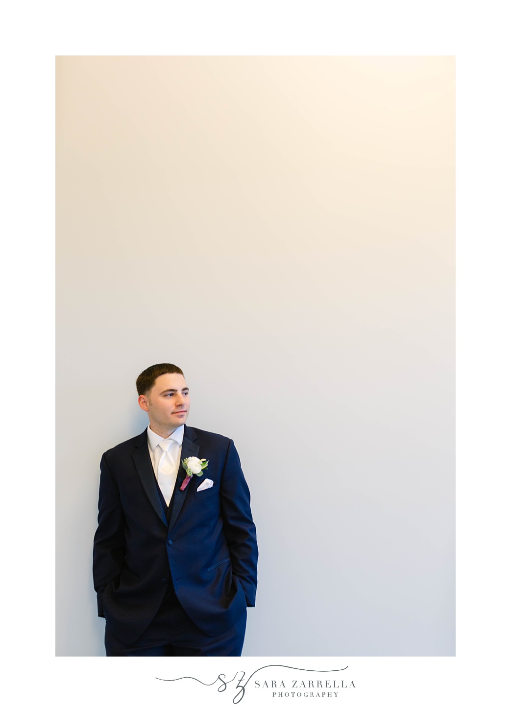 groom leans against white wall during RI wedding photos