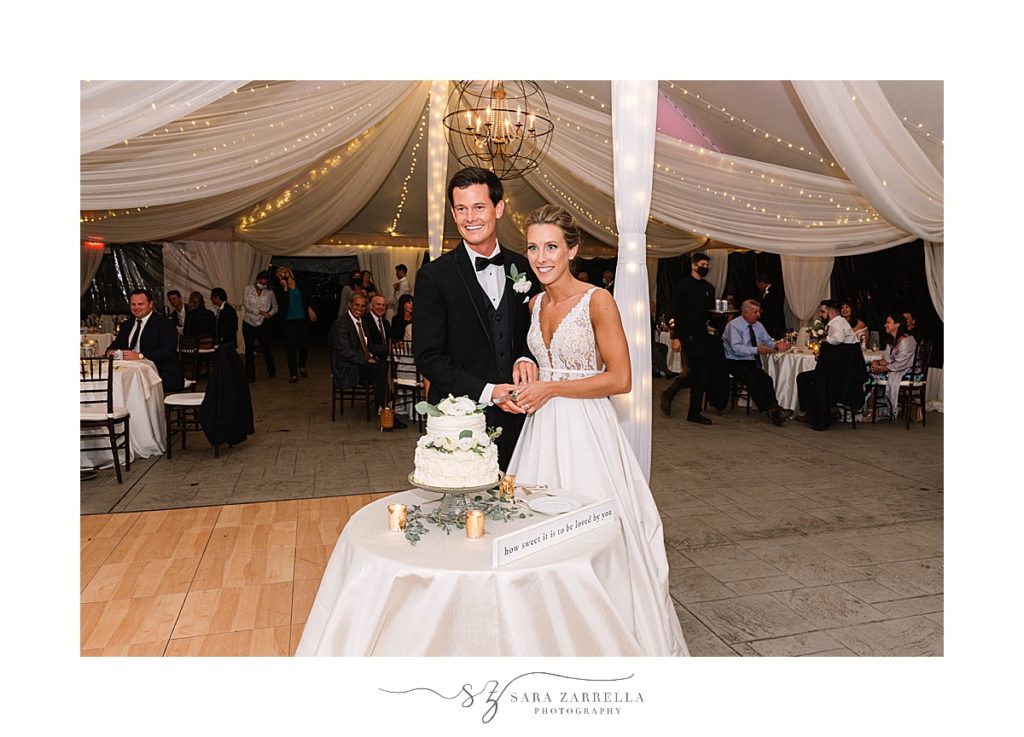 bride and groom pose by cake at reception