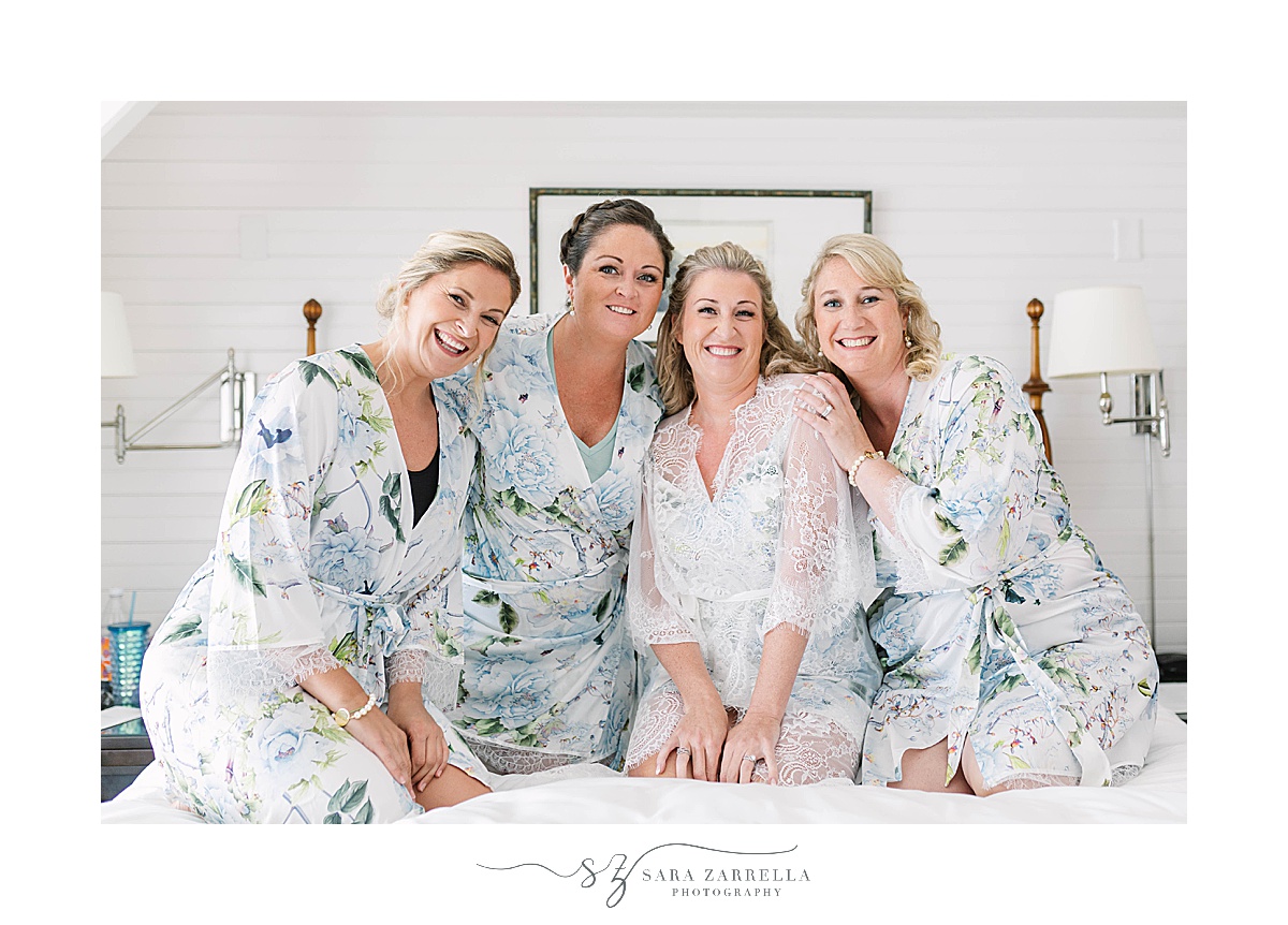 bride poses with bridesmaids in blue robes on bed