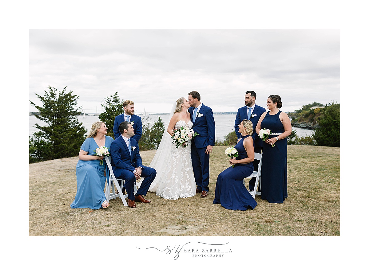 bridal party in blue dresses and suits watch newlyweds kiss