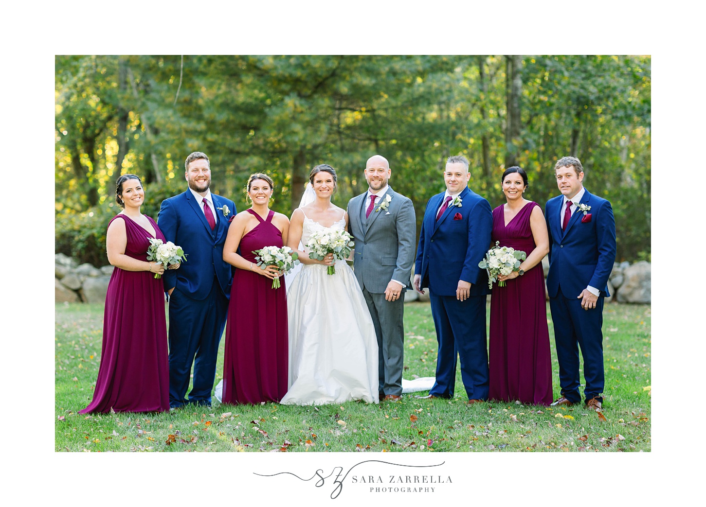 bride and groom pose with bridal party in burgundy gowns and navy suits