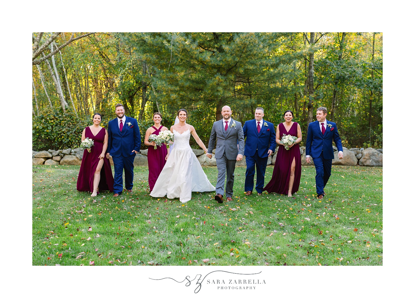 bride and groom walk with bridal party in burgundy gowns and navy suits