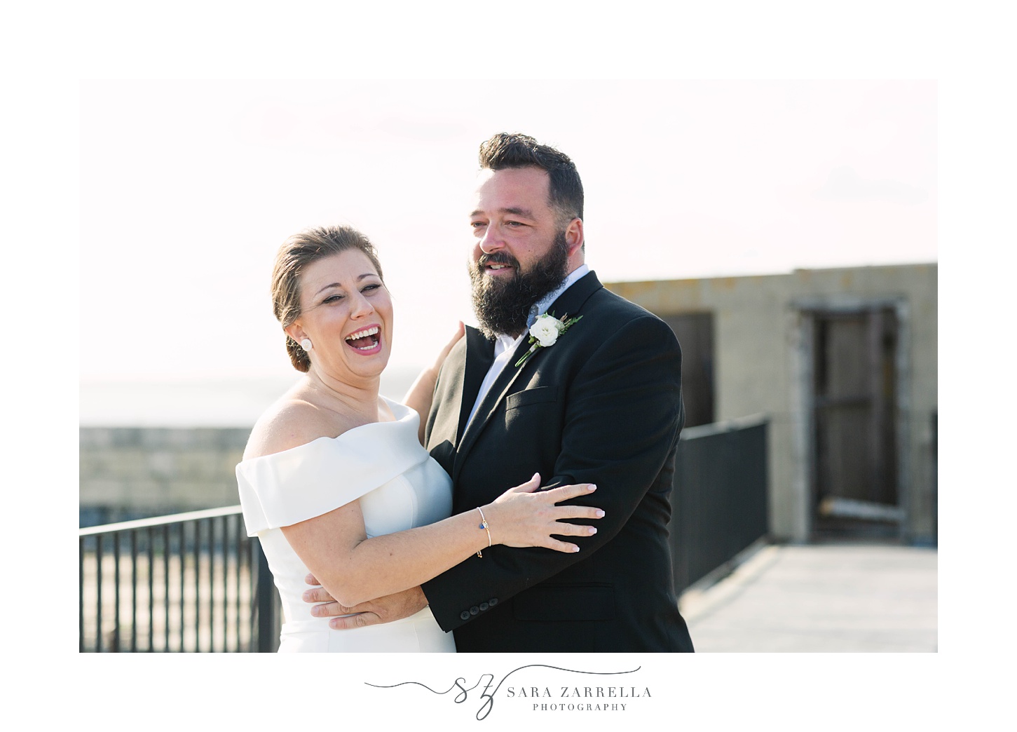 bride and groom laugh on top of Fort Adams during first look