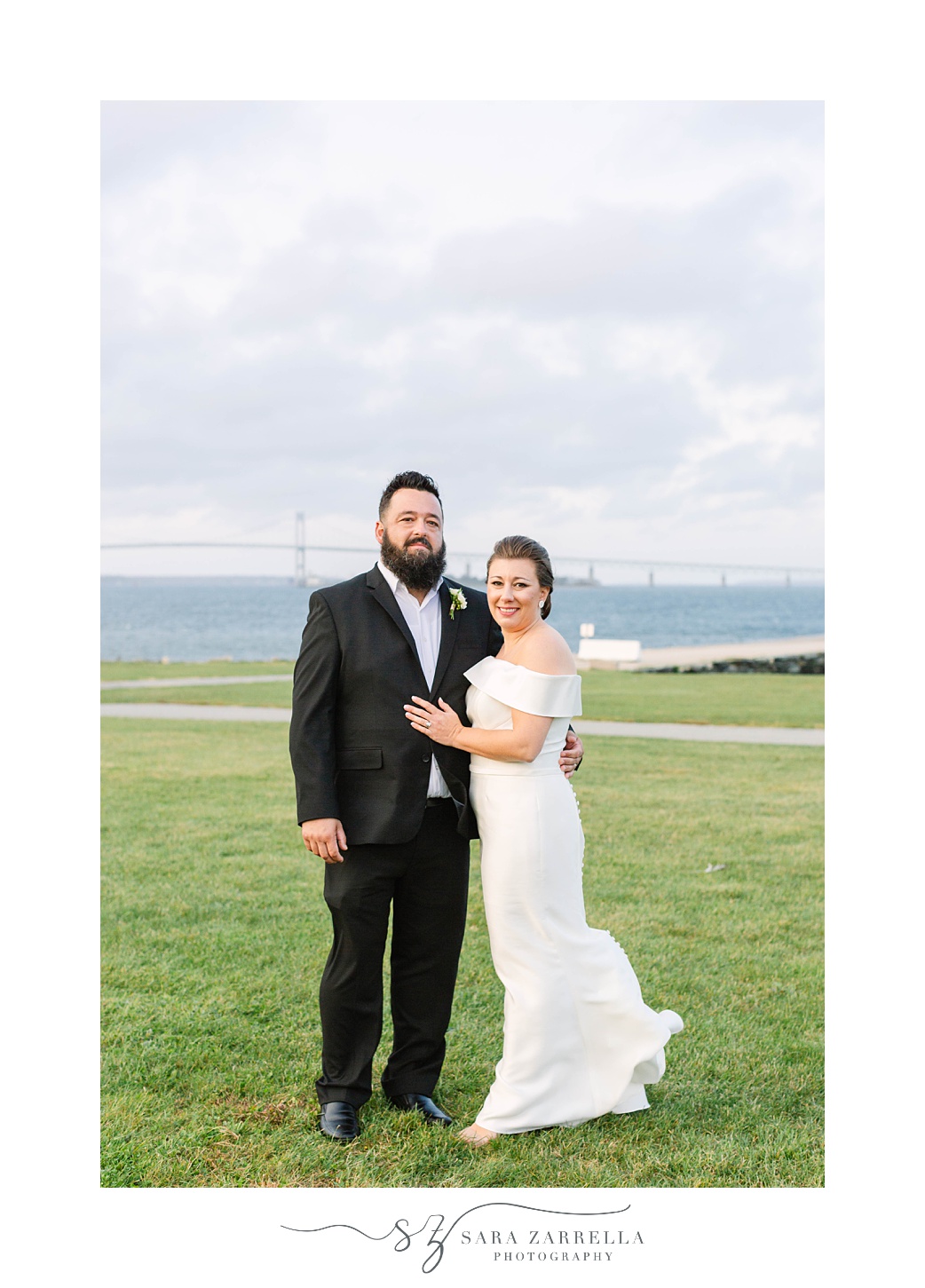 bride and groom pose in front of water outside Fort Adams