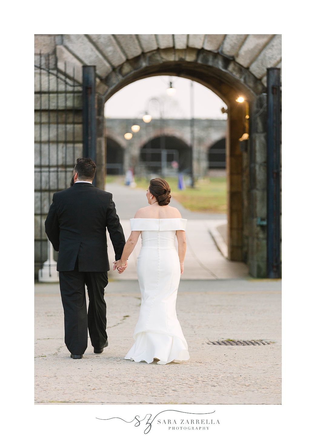 bride and groom walk into Fort Adams at sunset