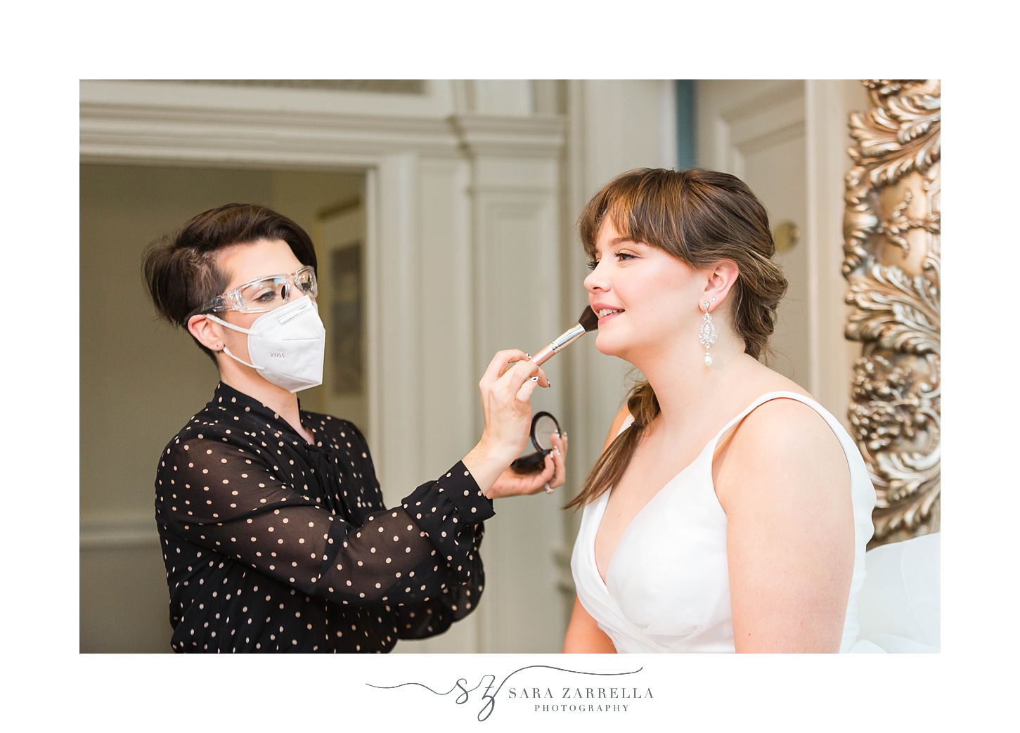 makeup artist prepares bride for wedding while wearing mask