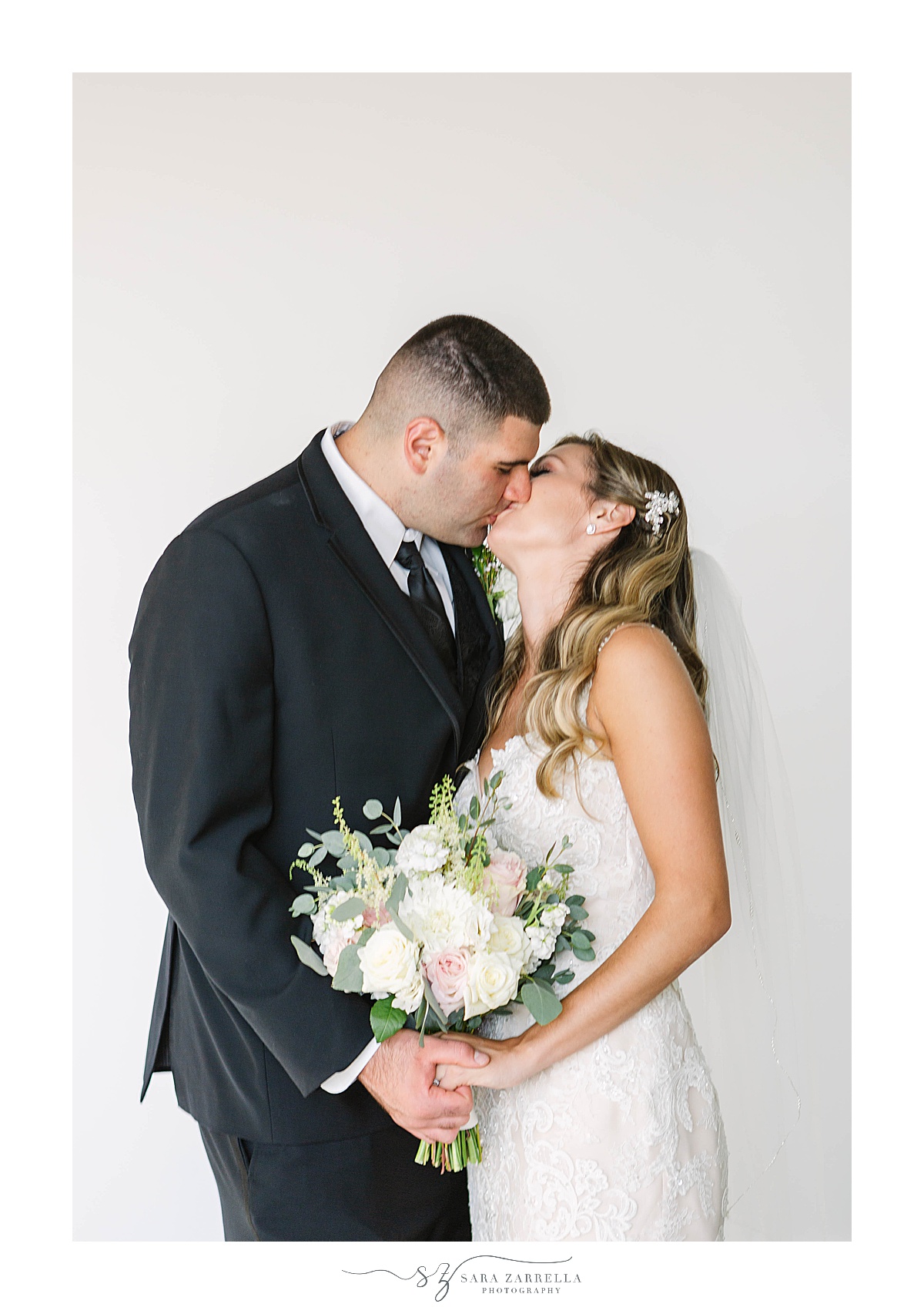 bride and groom kiss in front of white wall along Newport Beach House