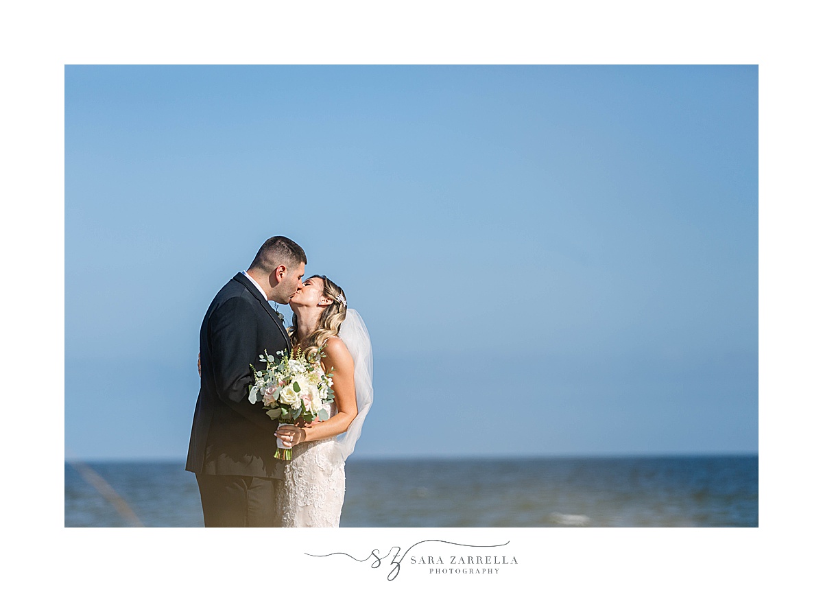 bride and groom kiss in front of blue sky in Newport RI