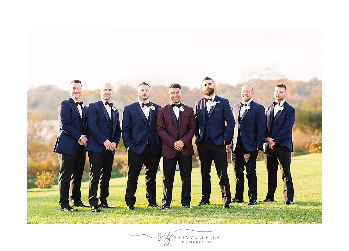 groom in burgundy suit and groomsmen in navy suits pose at Atlantic Resort Newport 