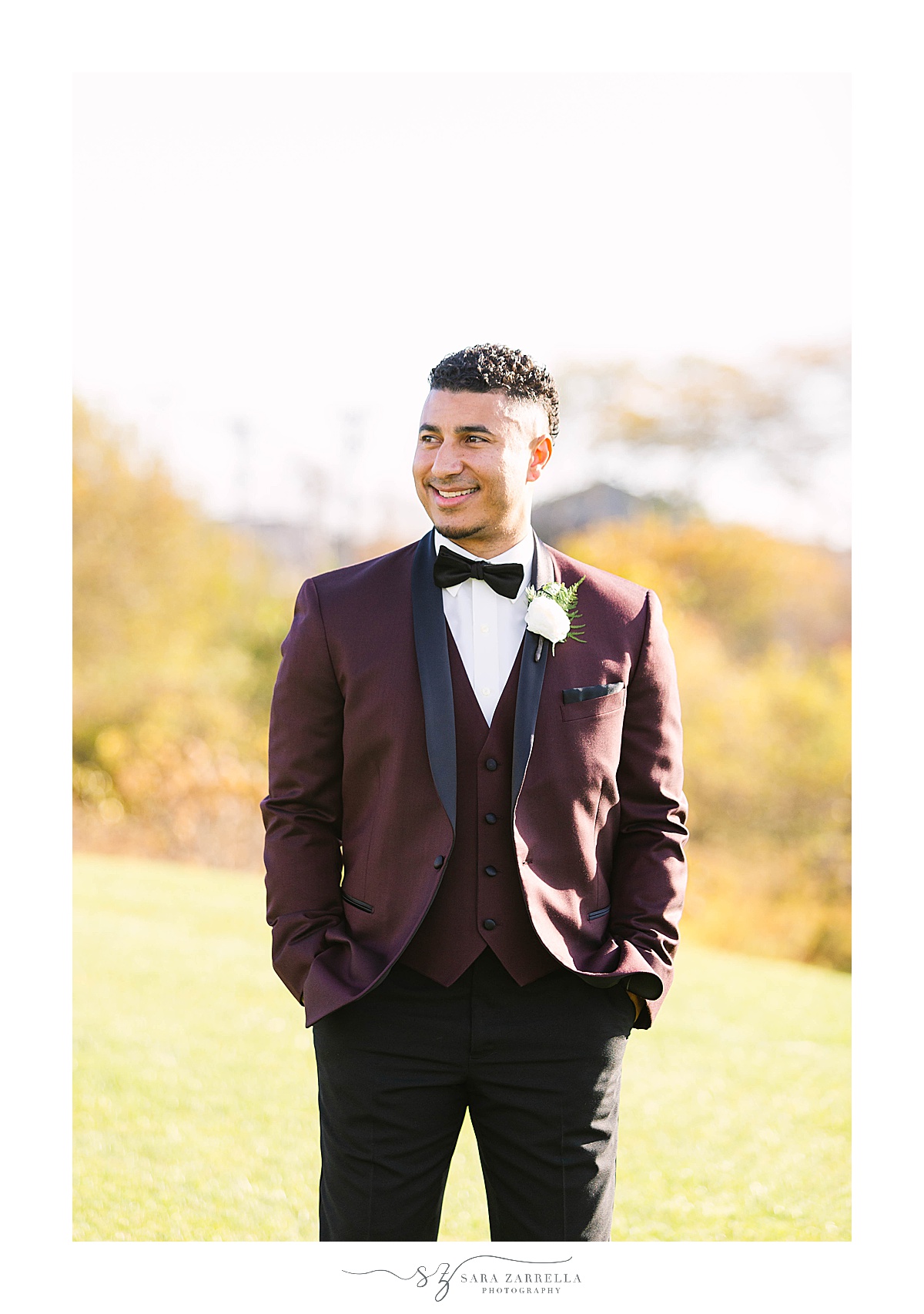 groom in burgundy suit jacket poses outside Atlantic Resort Newport 