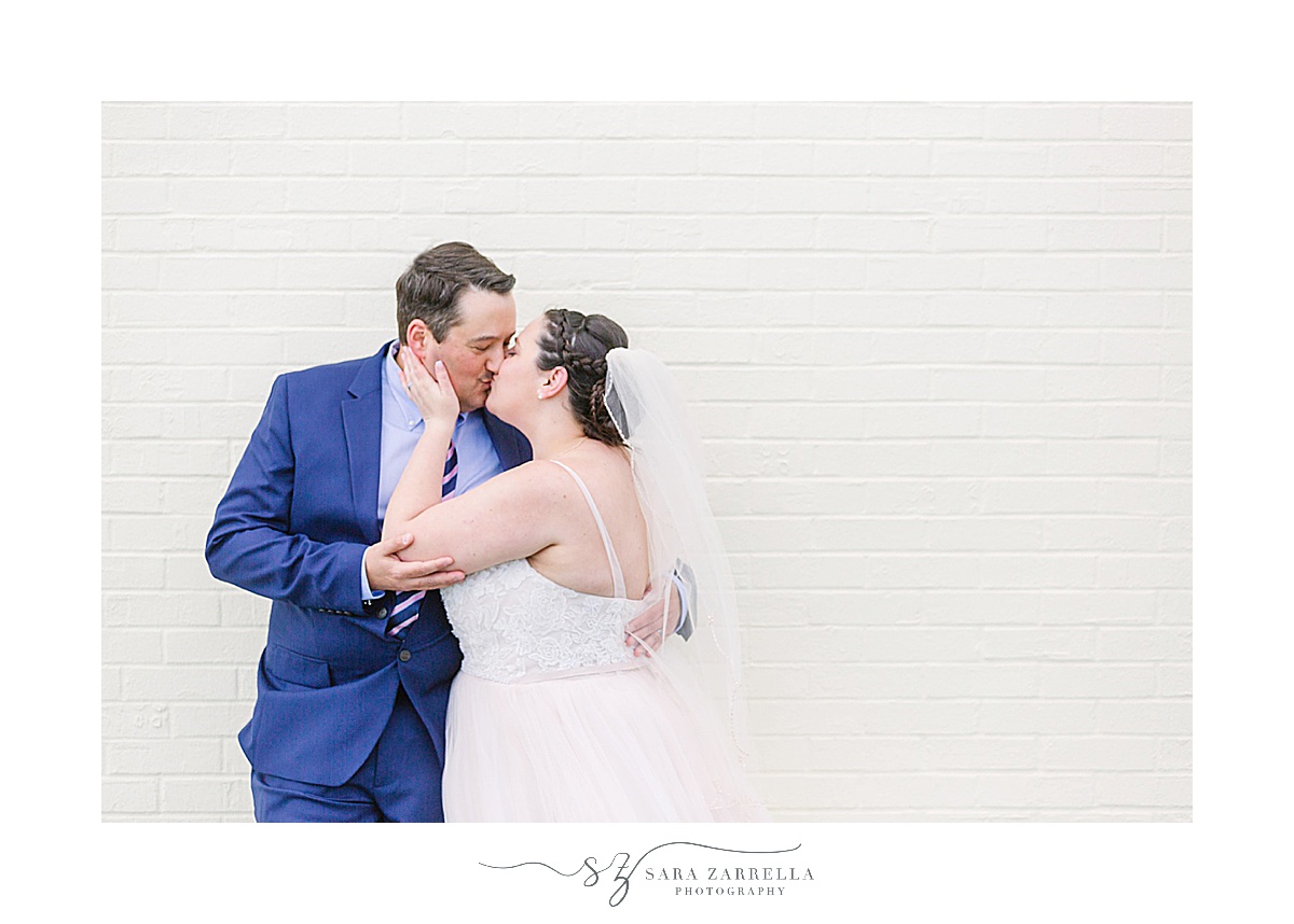 bride and groom kiss by white wall
