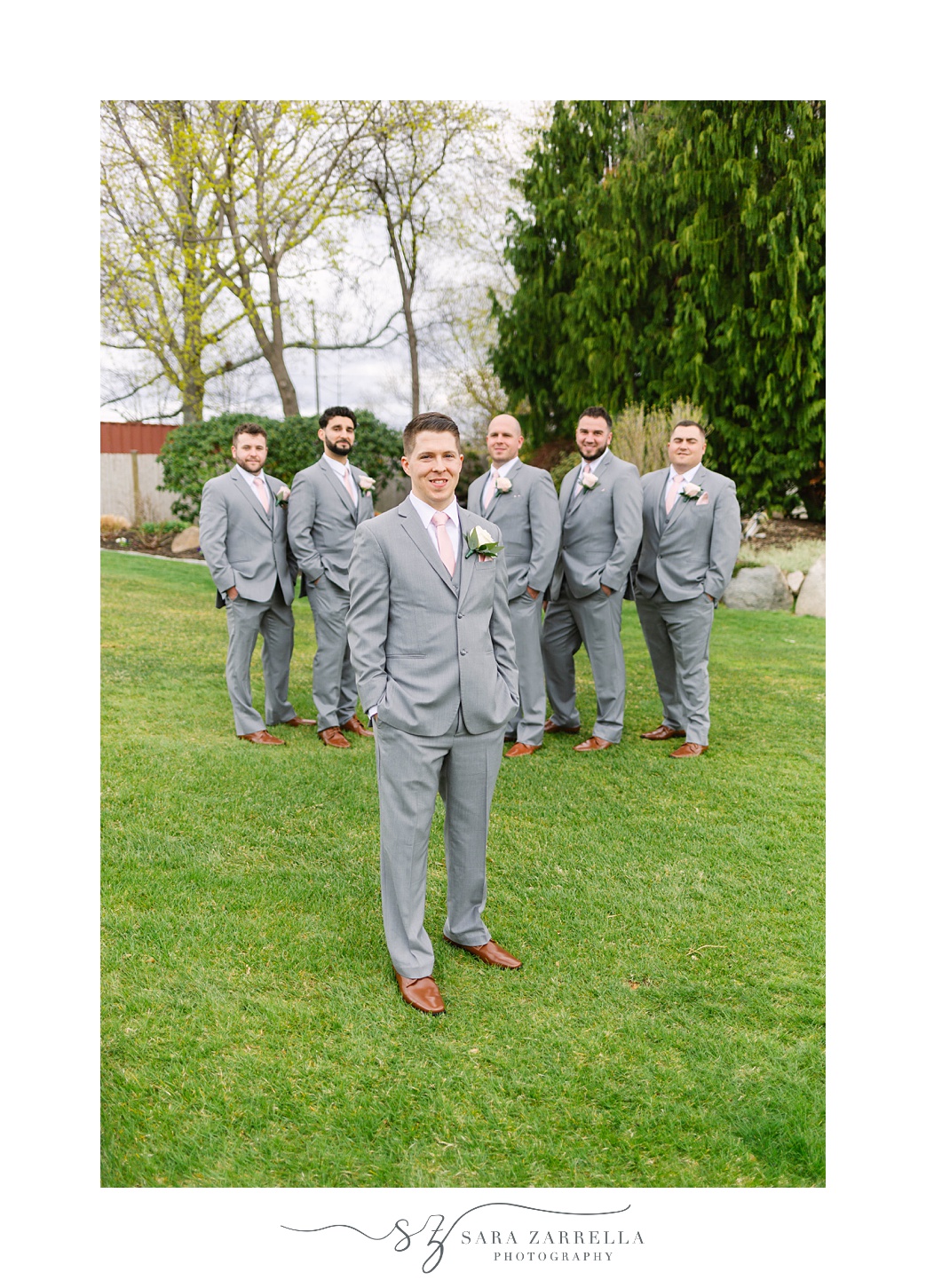 groom in grey suit poses with groomsmen behind him