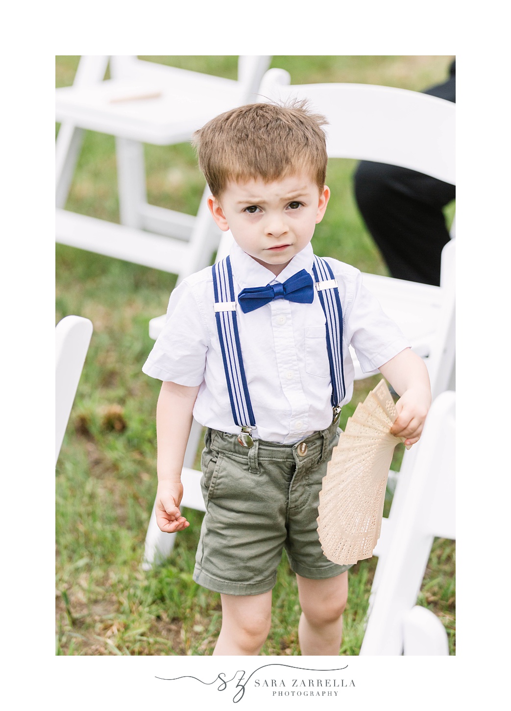 ring bearer in blue tie poses by white chairs for ceremony 