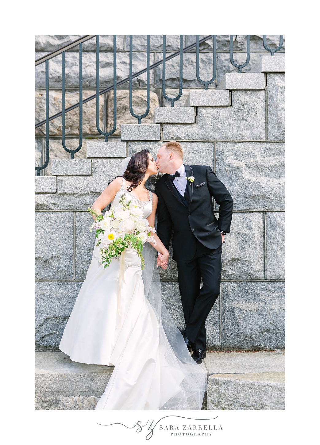 bride and groom hold hands kissing along brick wall in Providence RI