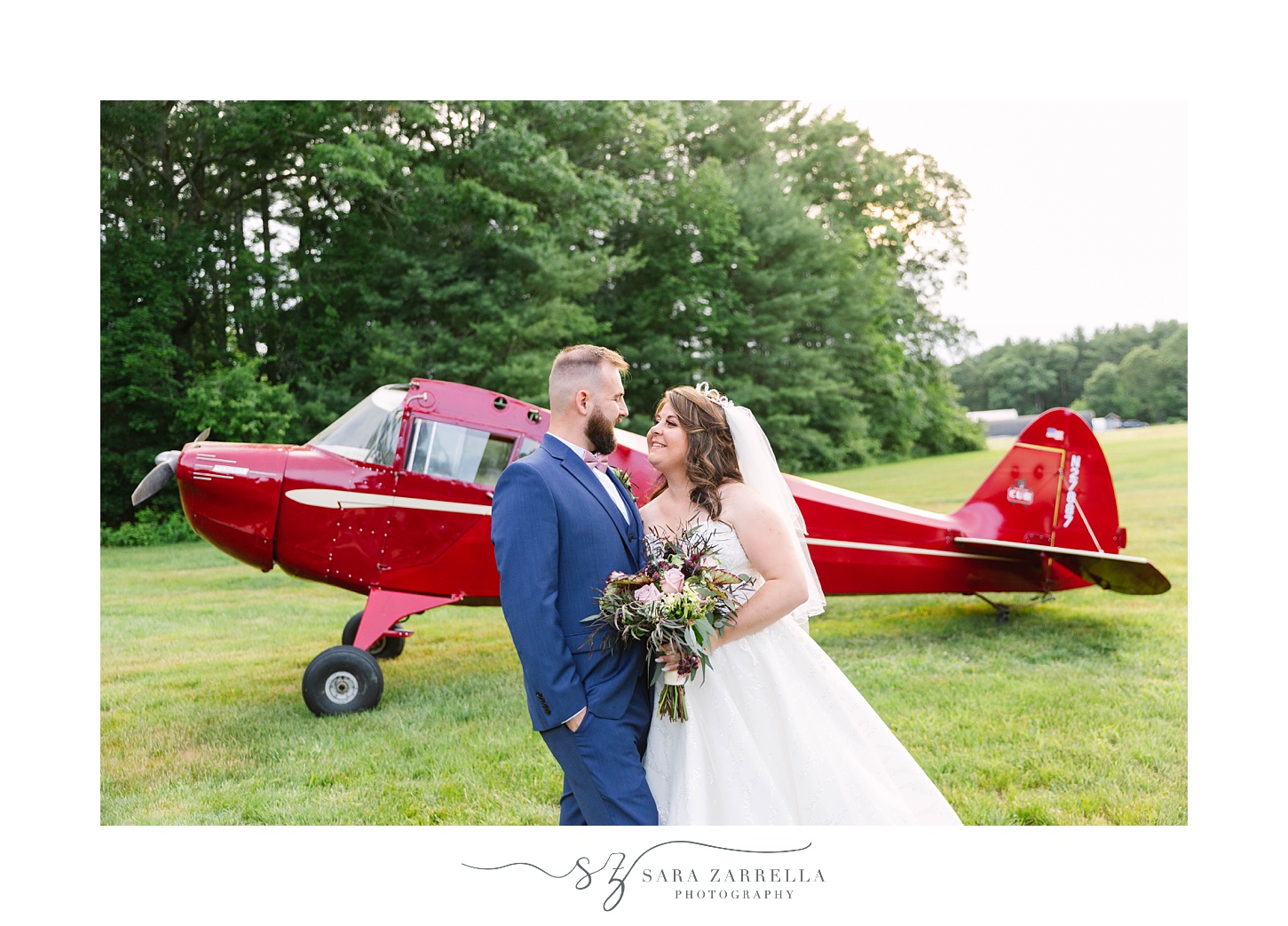 newlyweds pose by red airplane at Arch at the Meadow