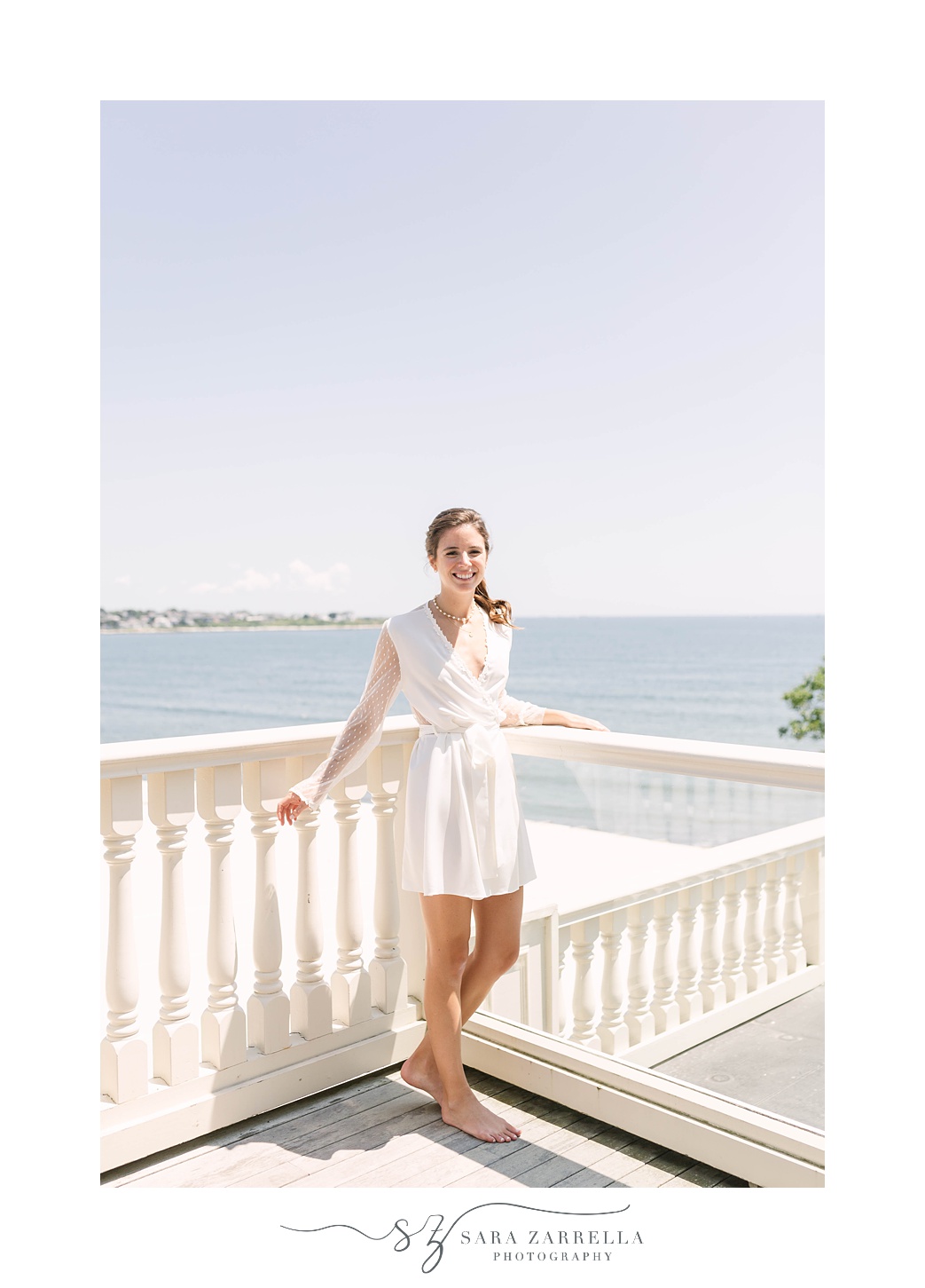 bride stands on patio at The Chanler at Cliff Walk overlooking the water in white robe