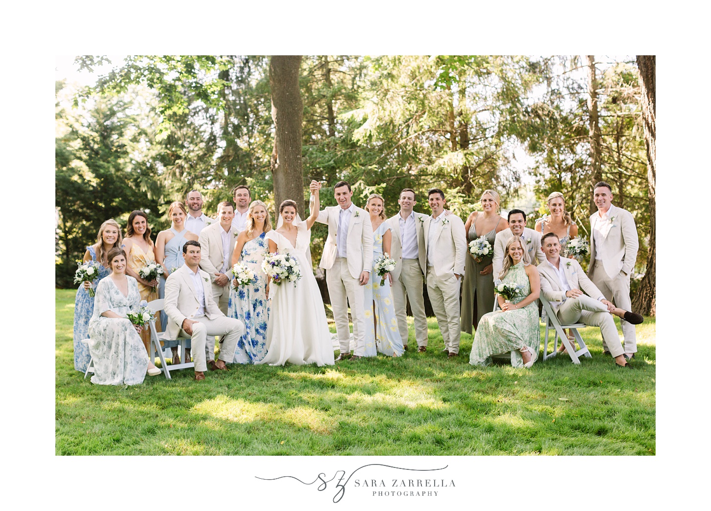 bride and groom pose with large wedding party in flower dresses and tan suits