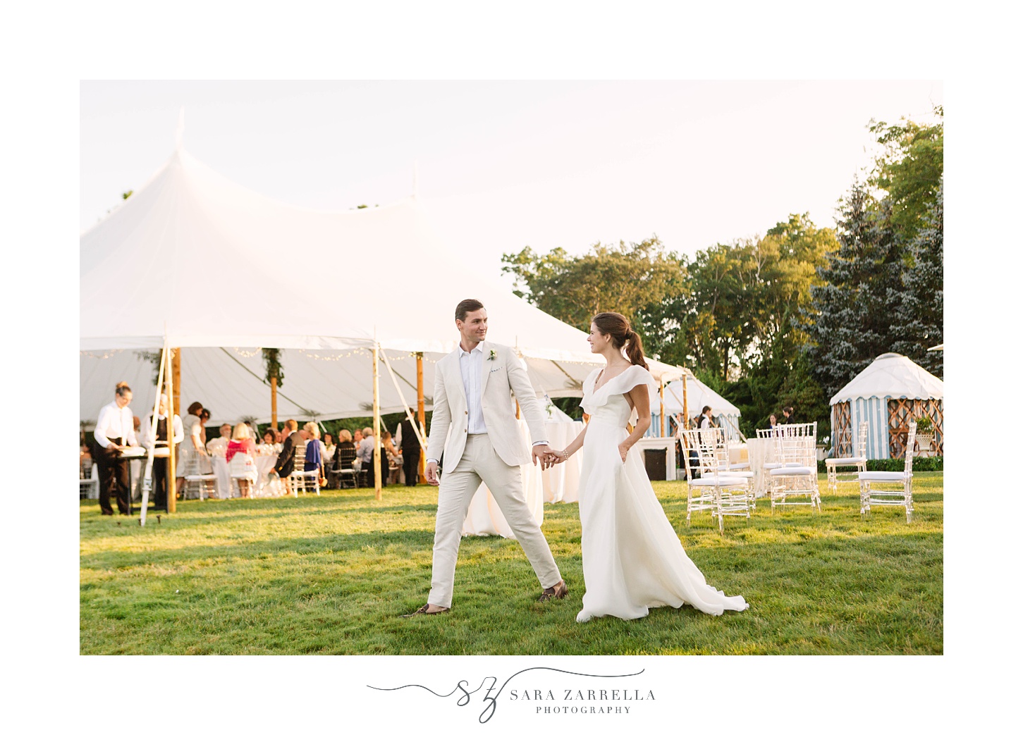 newlyweds hold hands walking by reception tent