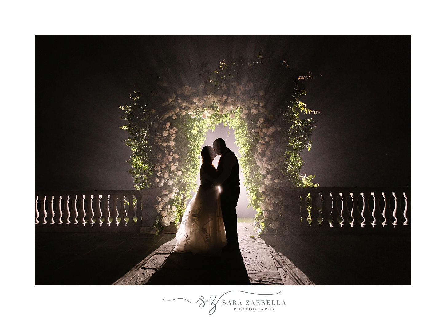 bride and groom kiss under greenery arbor at night 