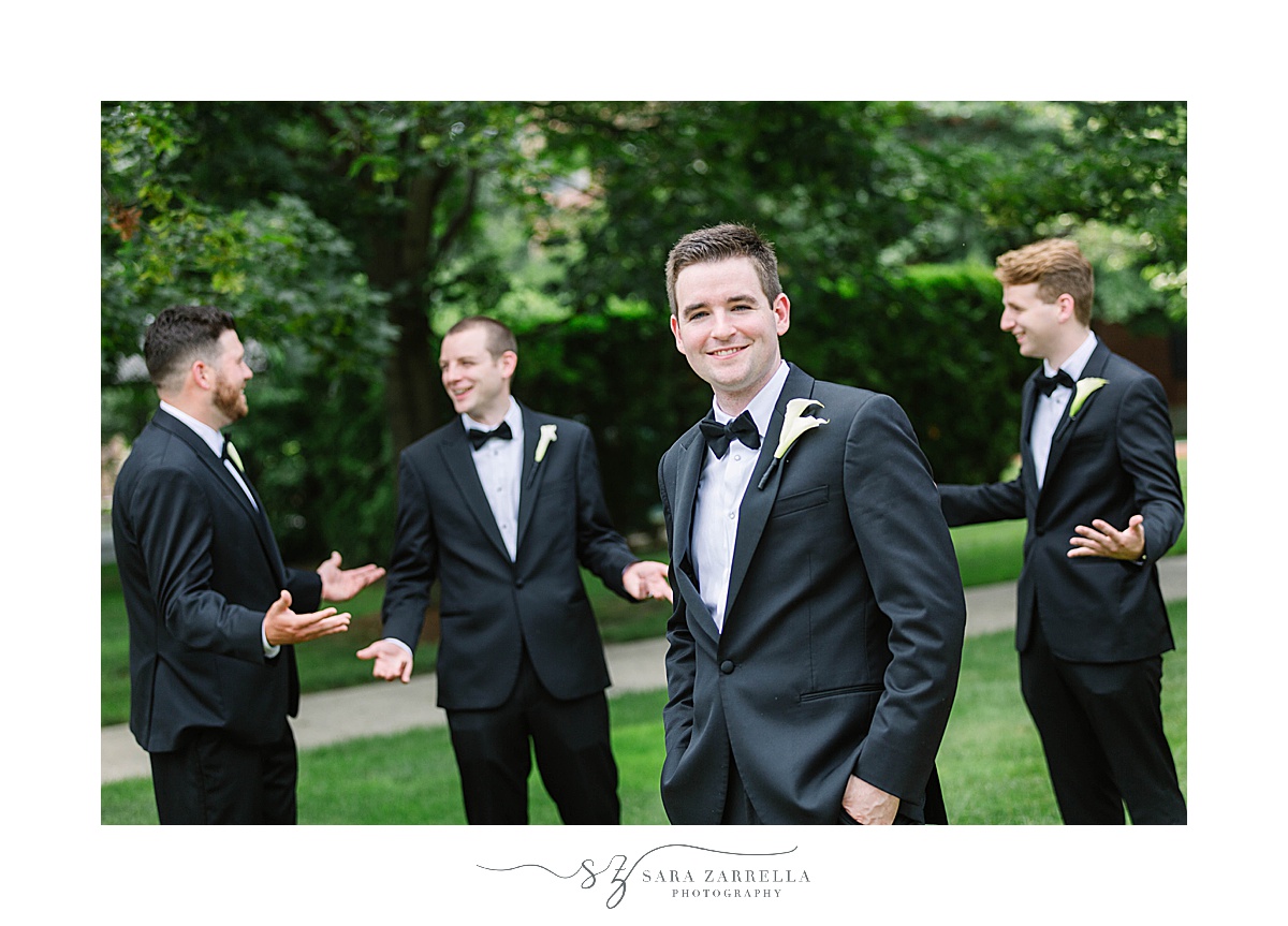 groomsmen laugh behind groom during portraits at Providence College
