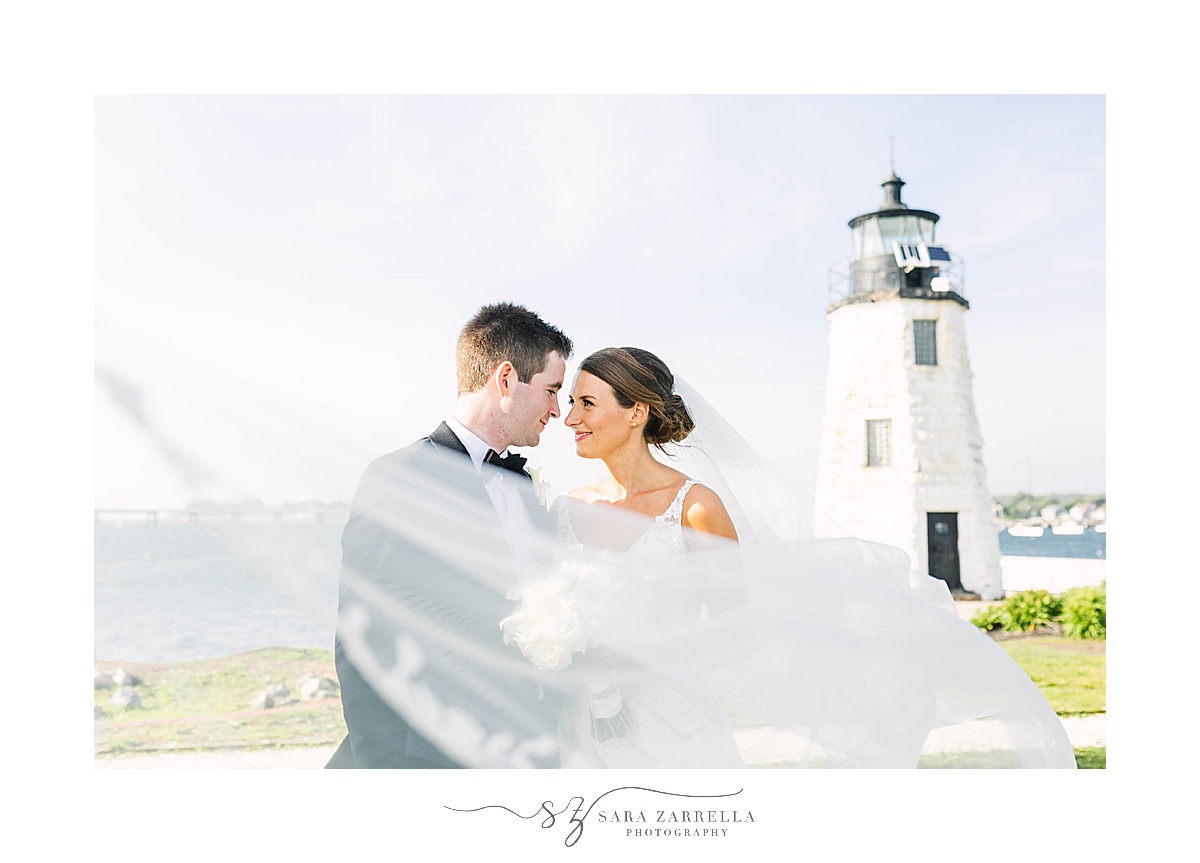 bride and groom kiss by lighthouse with veil floating 