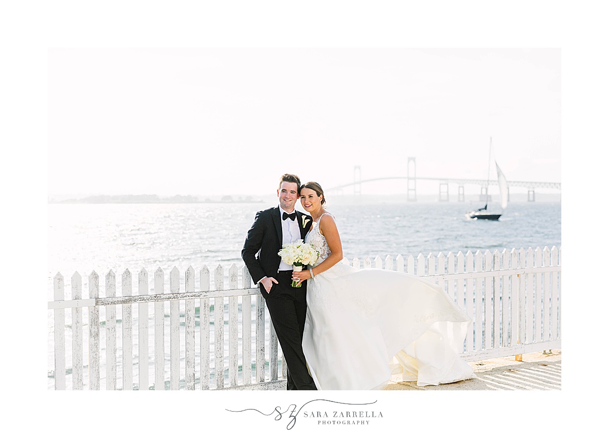 newlyweds pose by white fence outside Gurney’s Newport Resort