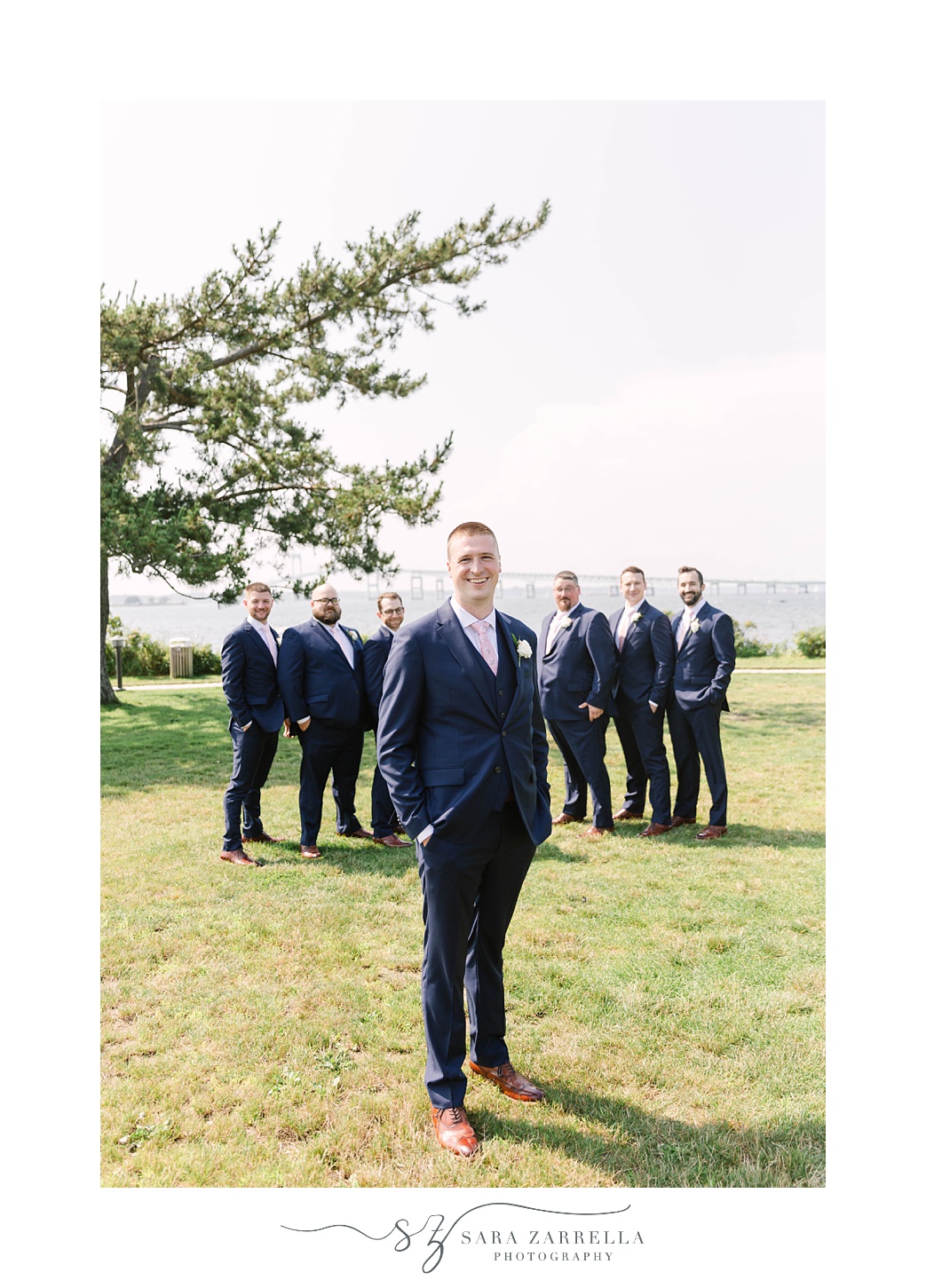 groom poses in navy suit with groomsmen on Gurney’s Newport Resort wedding day