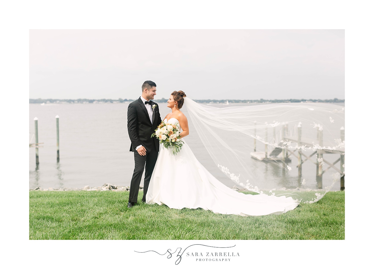 bride and groom smile along waterfront with bride's veil floating 