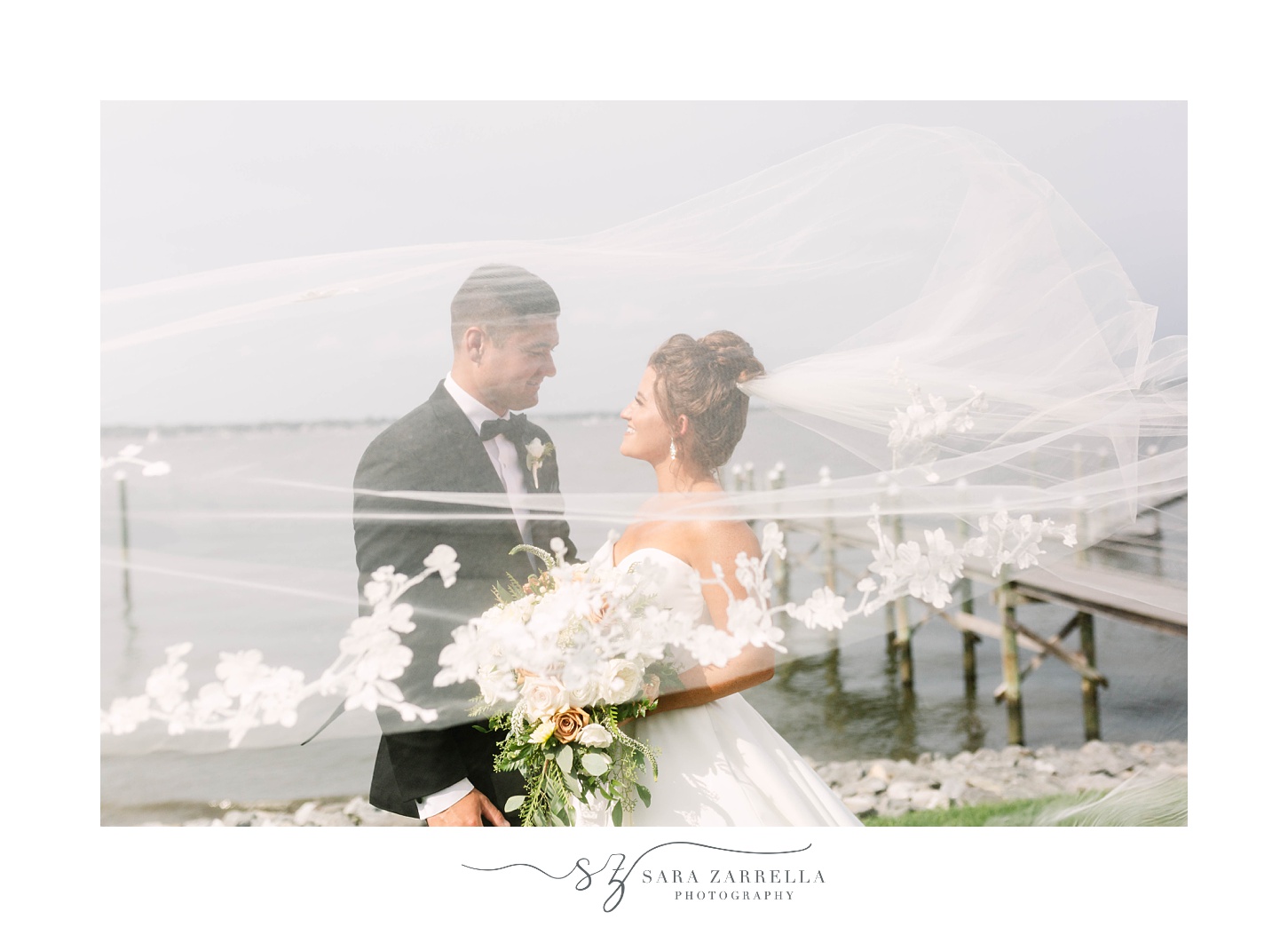 newlyweds pose by waterfront with veil floating