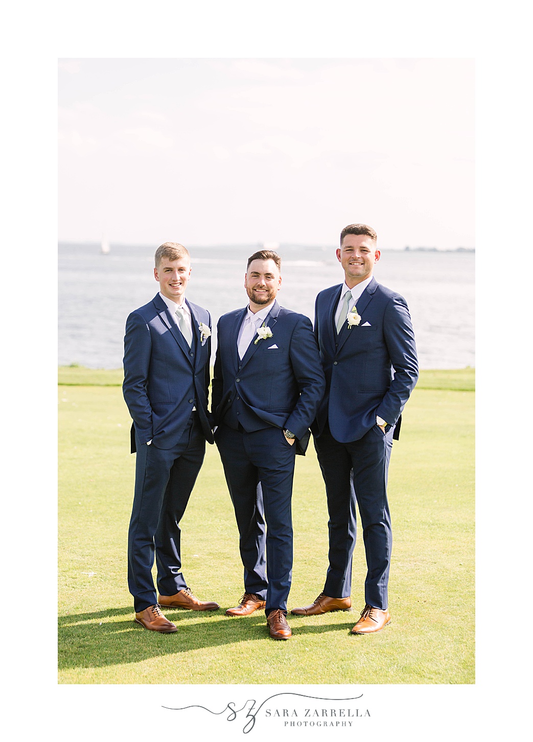 groom poses with two groomsmen in navy suits