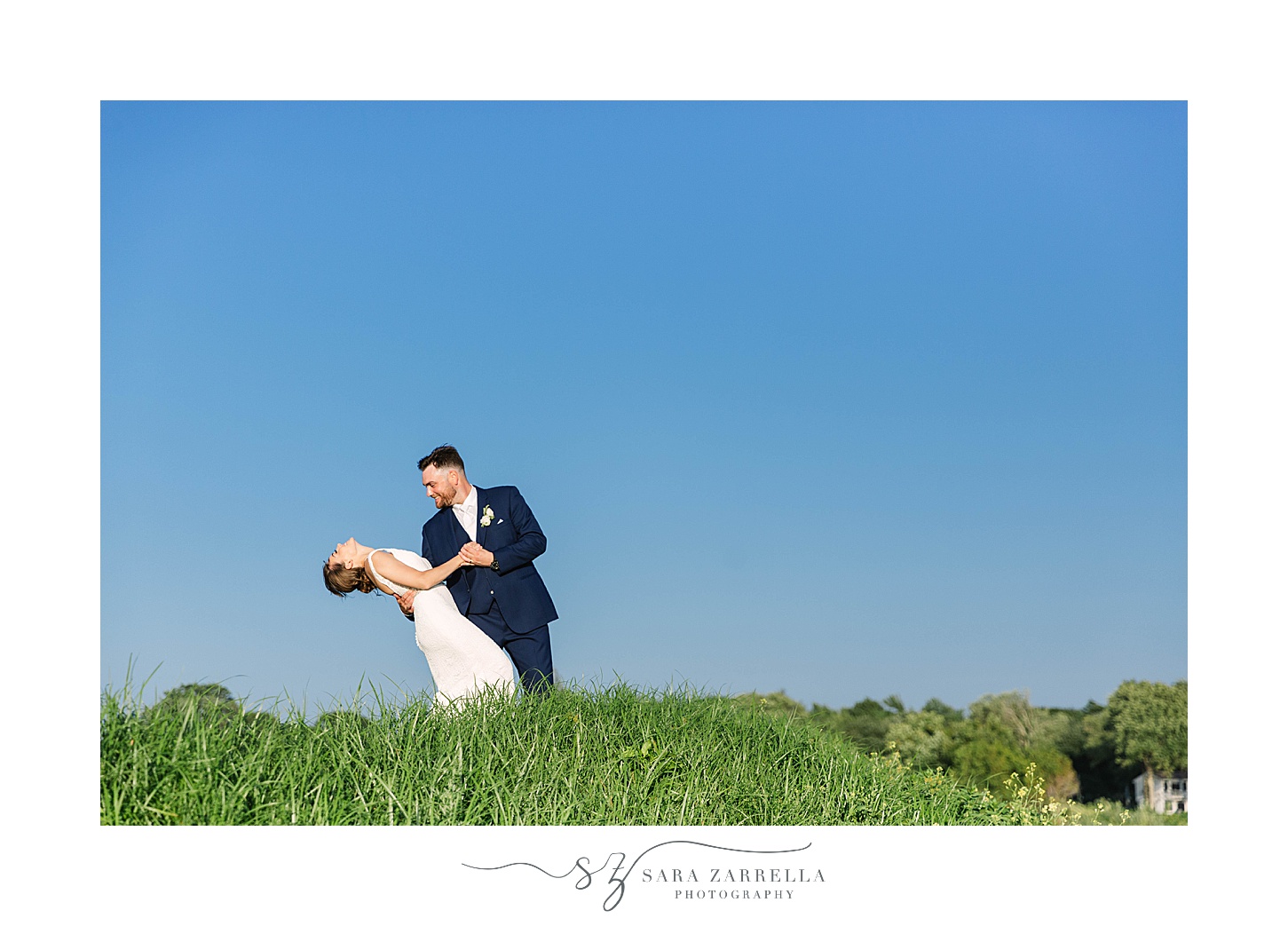 groom dips bride against blue sky in Warwick, RI