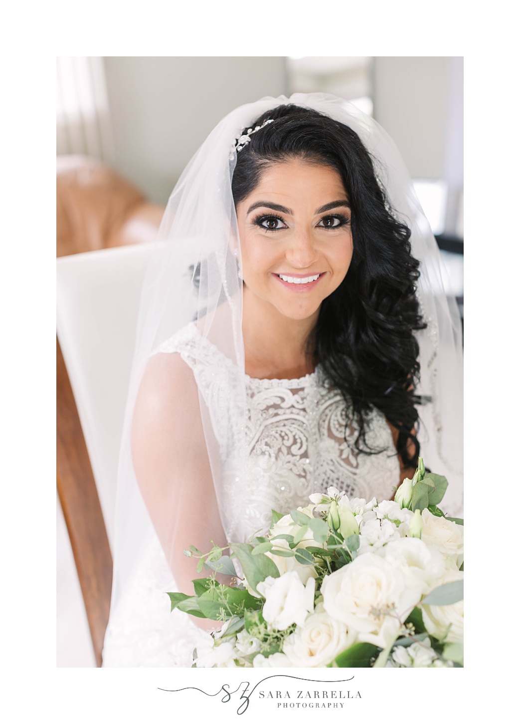 bride sits holding bouquet of white flowers with veil around shoulders 